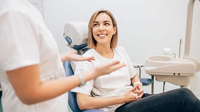 Lady with short blond hair sitting on a dental chair as a dentist speaks to her