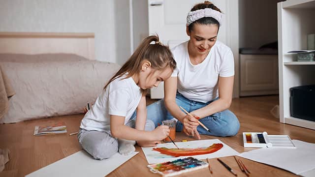 A mother and her daughter learning are coloring a picture in a bedroom