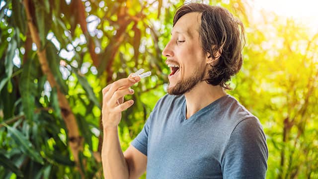 A man is placing a retainer in his mouth in an outside setting