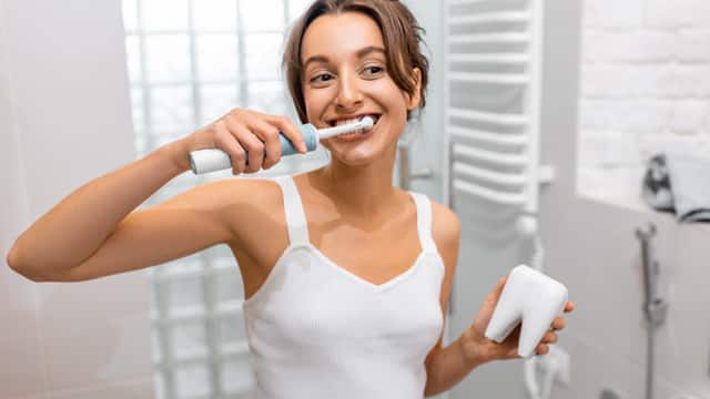 A young woman smiling and brushing her teeth in the bathroom while holding a tooth timer
