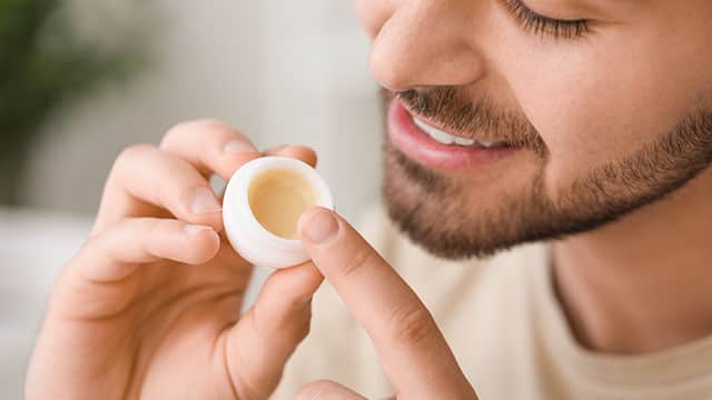 Closeup of a young man holding a ball-shaped lip balm at home