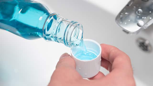 Close-up of a man's hands pouring mouthwash into a cap above the sink
