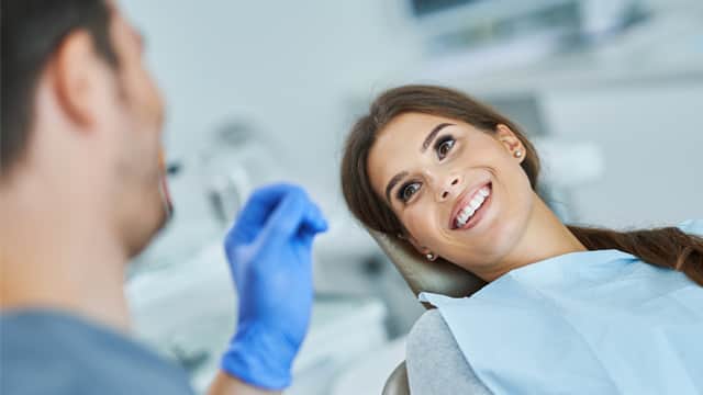 A male dentist talks with a smiling female patient in a dental chair