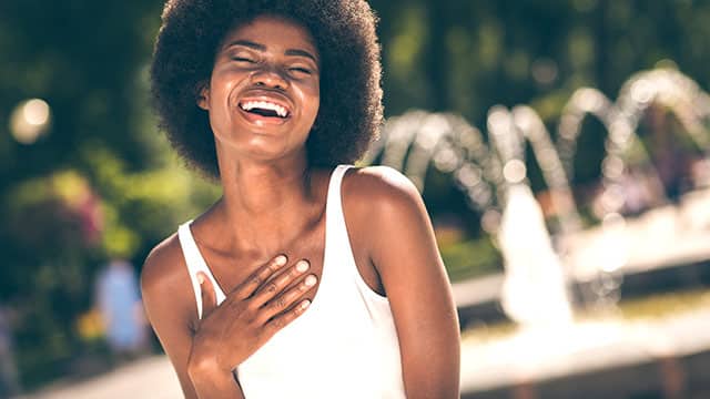 A positive cheerful afro American girl touching chest and laughing outdoors