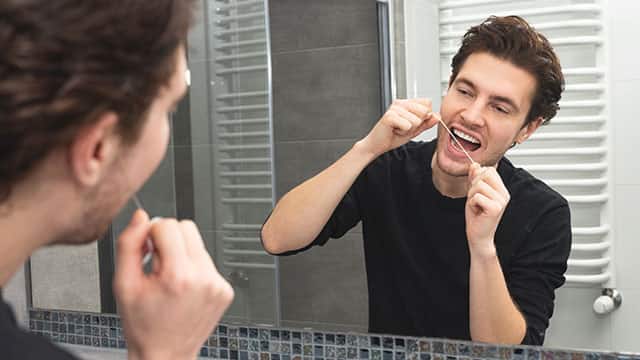 man using dental floss in front of bathroom mirror