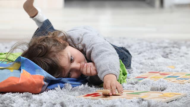 A toddler playing and laying down on a rug while sucking their thumb