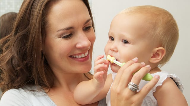 A smiling mother brushing her baby's teeth in a bathroom