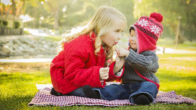 Little Girl with Baby Brother enjoying lollypops Outdoors
