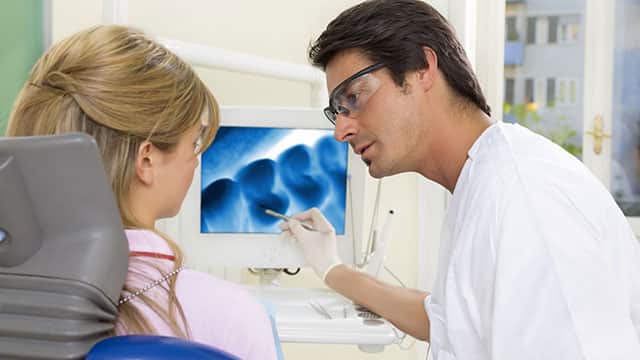 A dentist is talking and showing an x-ray to the patient in dental office