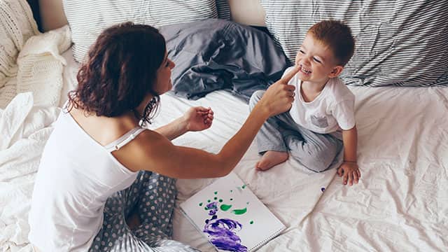 A mom relaxing with her little son in a bedroom while painting 
