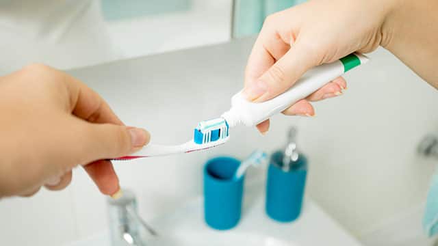 Closeup of woman putting toothpaste on toothbrush at bathroom