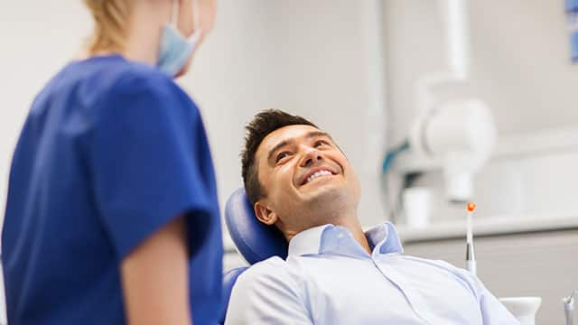 man sitting on dental chair smiling at the dentist assistant