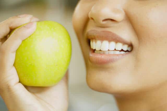 Ciérrese para arriba de la mujer que sostiene la manzana al lado de su boca