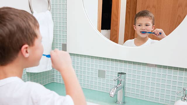 A kid is brushing his teeth in front of the mirror