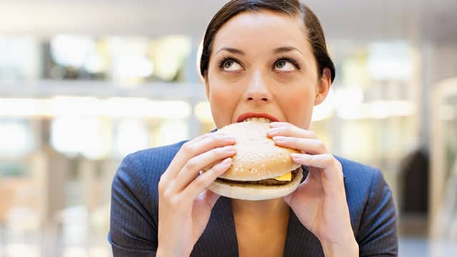 a woman in navy suits is eating burger indoors