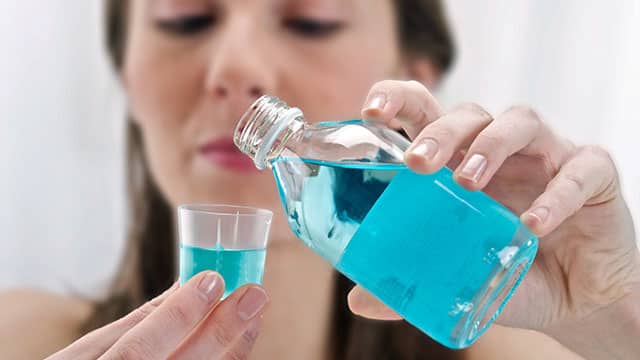 Close up of the woman's hand pouring mouthwash in to the cup Close up of the woman's hand pouring mouthwash in to the cup