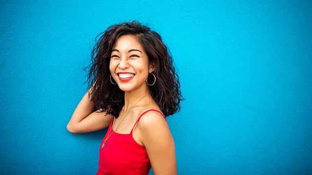 A portrait of a smiling woman outdoors in a red shirt in front of a blue wall