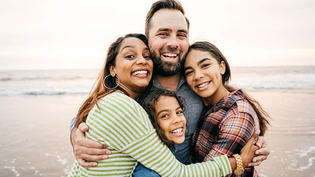 a happy family hugging and smiling together at the beach