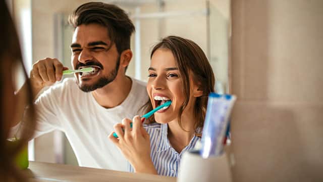Image of the young couple in the mirror brushing their teeth