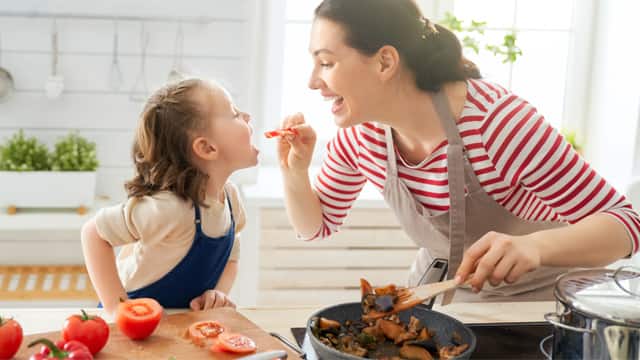 A mother and daughter taste-test a meal while cooking in the kitchen