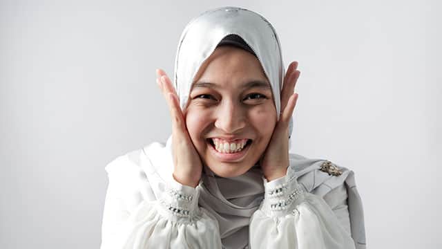 Young woman in head scarf is smiling and holding her cheeks