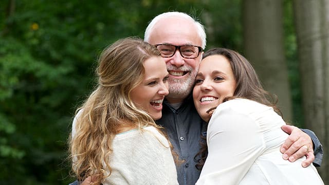 Father hugging his daughters Smiling father hugging his two daughters