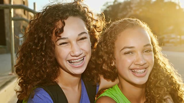 Two teenage girls with braces smiling outside