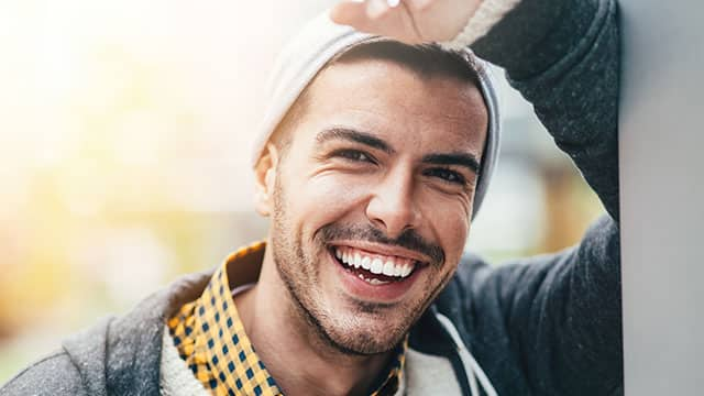 Smiling man wearing a hat with a yellow checkered shirt and white sweater