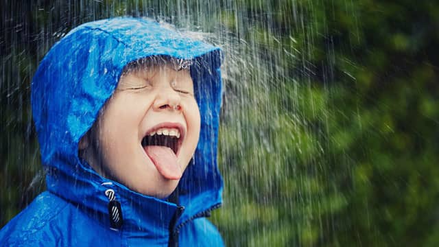 A little boy in a blue rain jacket catching rain drops on his tongue