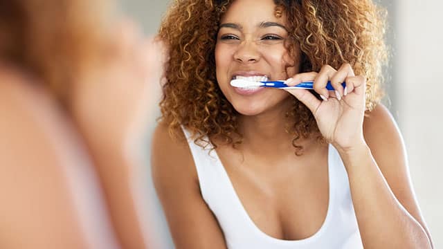 Woman brushing her teeth in the bathroom mirror