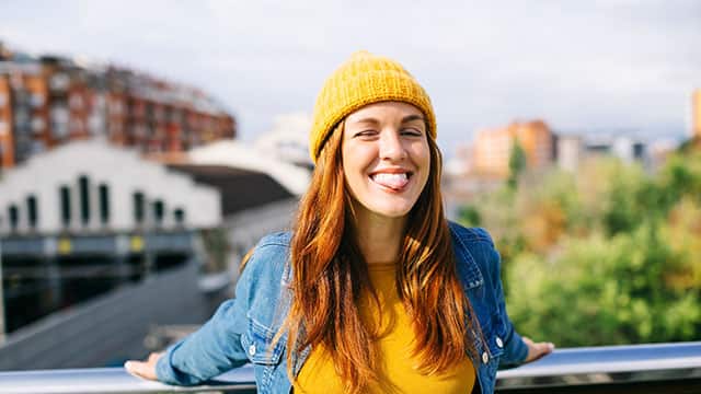 Young woman in a yellow cap and denim shirt on bridge smiling and sticking out her tongue