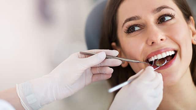 a woman is sitting in a chair and her teeth is being examined by dentist