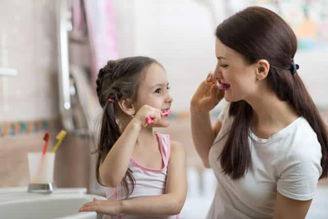 Niña pequeña y mamá cepillarse los dientes en el baño