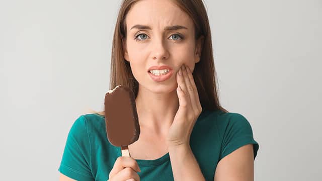  Lady showing discomfort from sensitive teeth after biting into an ice cream