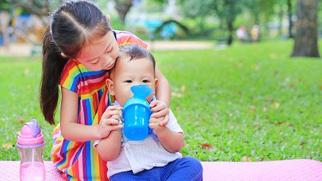 Sister helping her brother use sippy cup