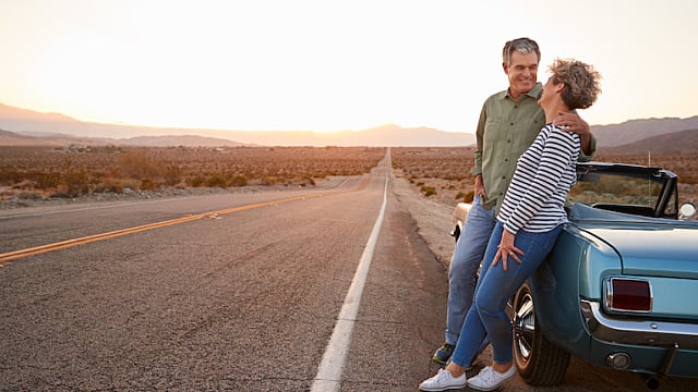 Senior couple on road trip standing by car, full length