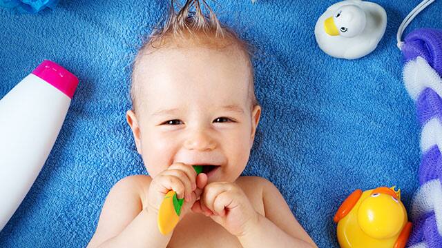 Baby laying down and smiling with a toy in their mouth