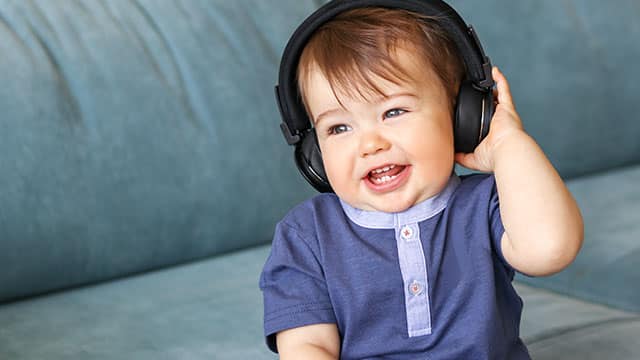 A baby is listening to music in headphones Little baby boy listening to music in headphones and smiling with his baby teeth