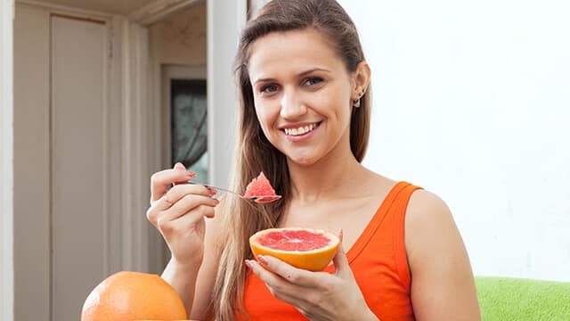 woman eating grapefruit with spoon at home