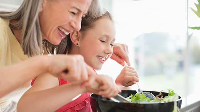 Grandmother and granddaughter smiling while preparing a salad