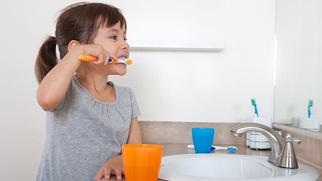 a girl looking at the mirror while brushing her teeth with Colgate toothbrush