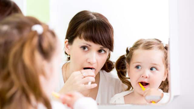 Madre enseñándole a su hija a lavarse los dientes