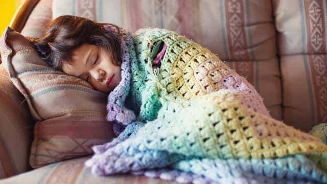 A girl covered with a blanket sleeping on a sofa