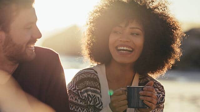 woman and a man smiling outdoor while enjoying a cup of coffee