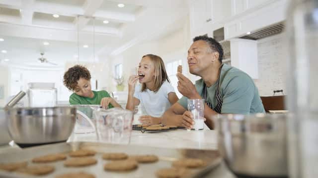 A father, daughter and a son in the kitchen enjoying a tray of cookies
