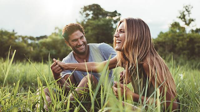 Couple laughing in grassy field on sunny day