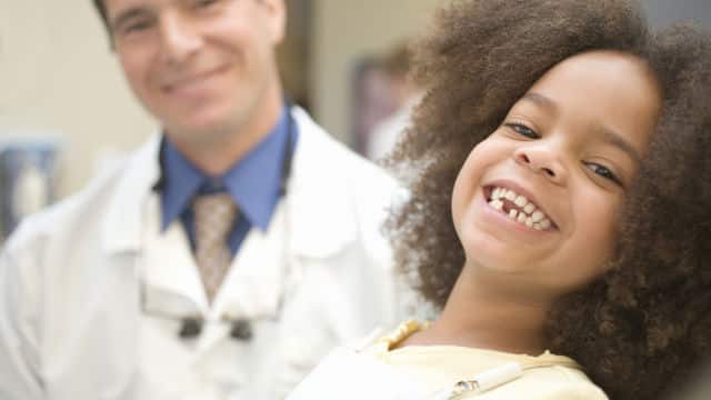 a girl smiling next to the dentist with her bottom tooth missing