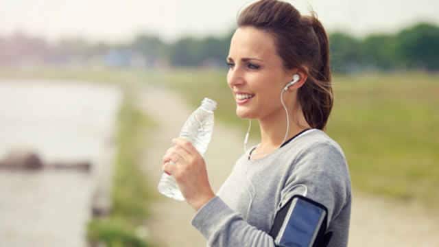 Smiling woman holding a water botter while listening to music jogging
