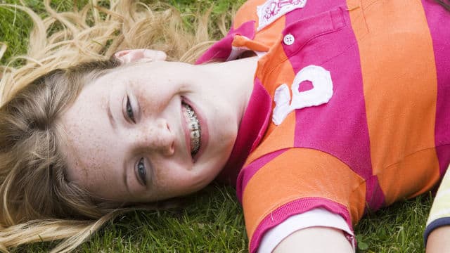 a girl with braces smiling brightly laying on the grass
