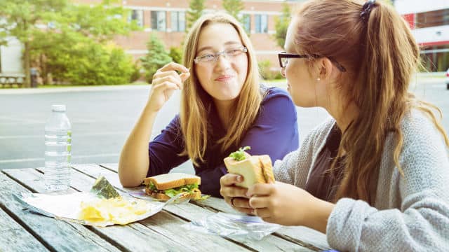 two woman smiling while eating a sandwich